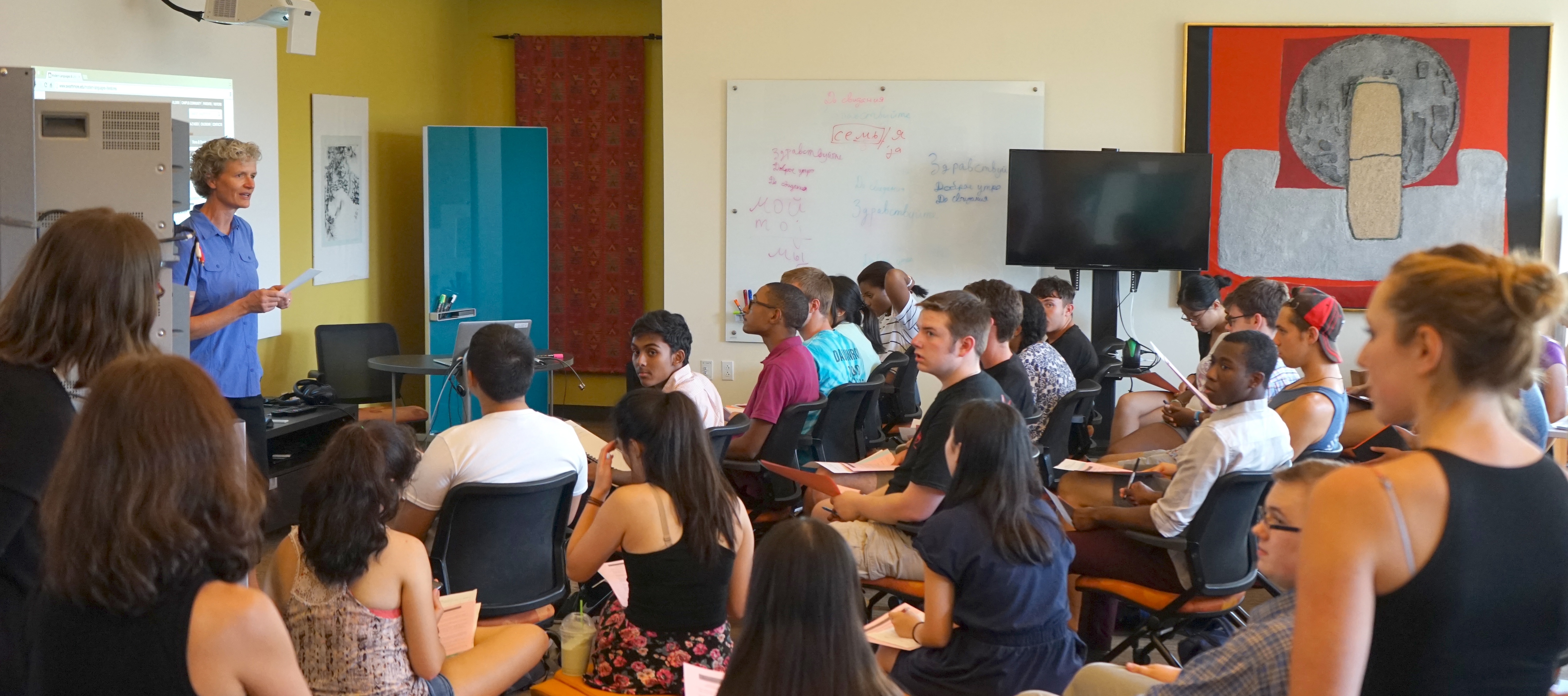 A faculty member presenting to a large group of students sitting and standing the Language Center.